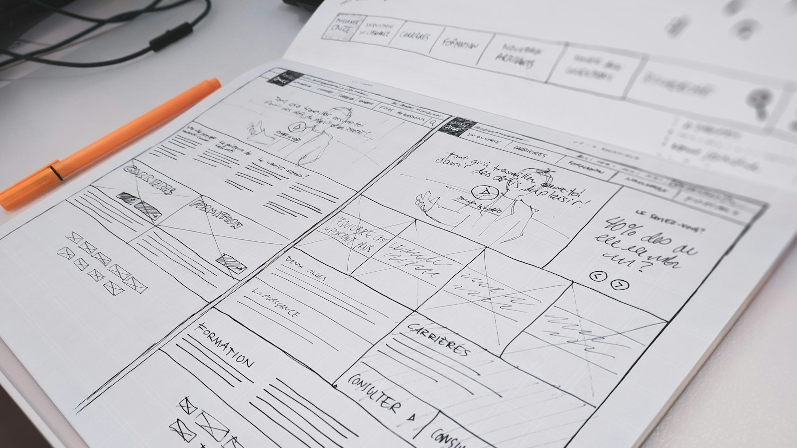 Hand-drawn website wireframes beside an orange pen